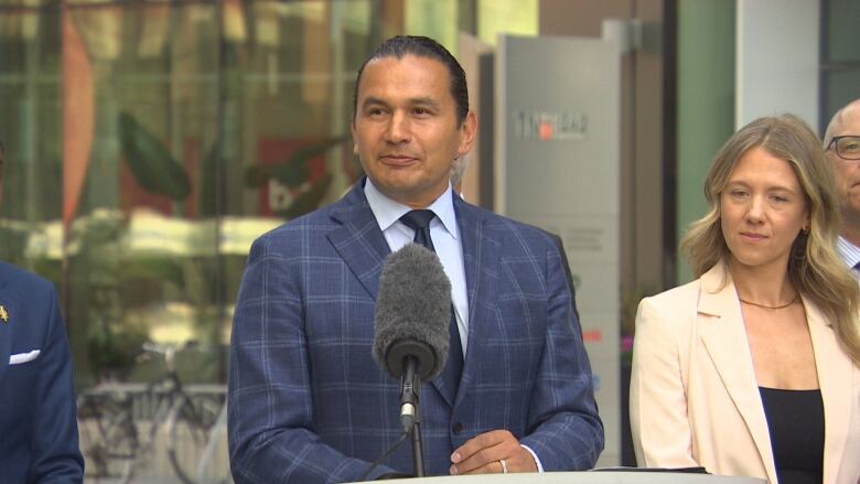 A man in a suit speaks at a podium in front of a building.