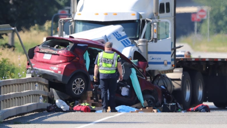 A red car is totaled and sitting on a barrier, in front of a white-and-blue tractor trailer. 