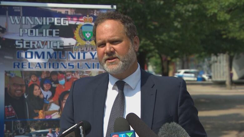 A man in a suit speaks into microphones at an outdoor podium