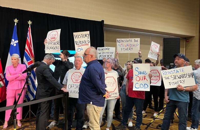 Protesters hold posters inside a hotel ballroom.