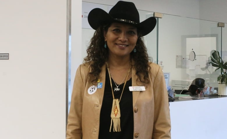 A woman stands in front of a front desk, with part of a sign saying 