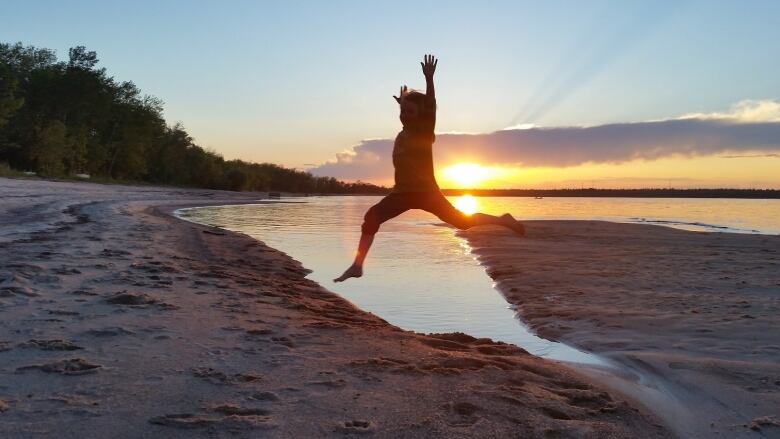 A person is silhouetted as they jump on a beach in the sunset