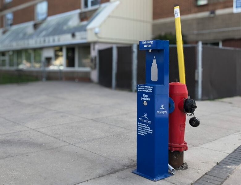 A fire hydrant is seen connected to a blue water drinking station.