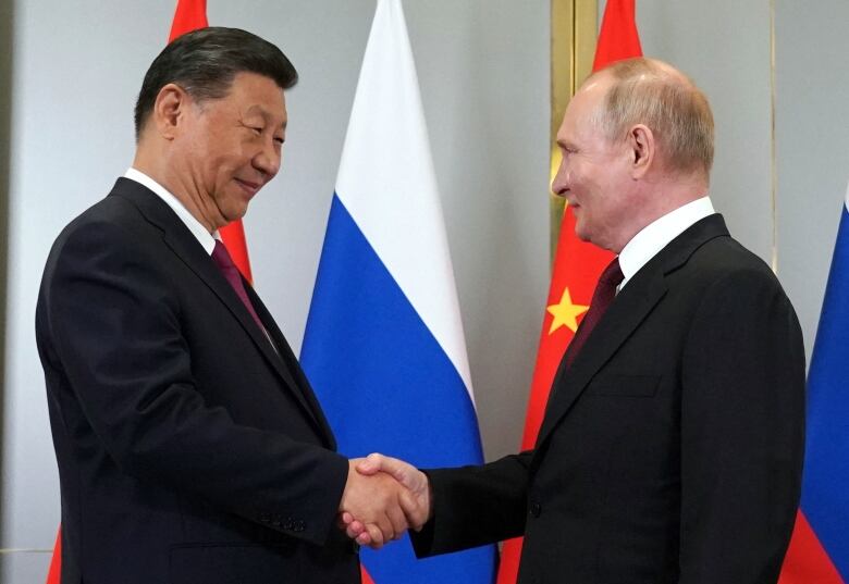 An Asiatic man and a Caucasian man in suits and tie shake hands at what appears to be an official government function.