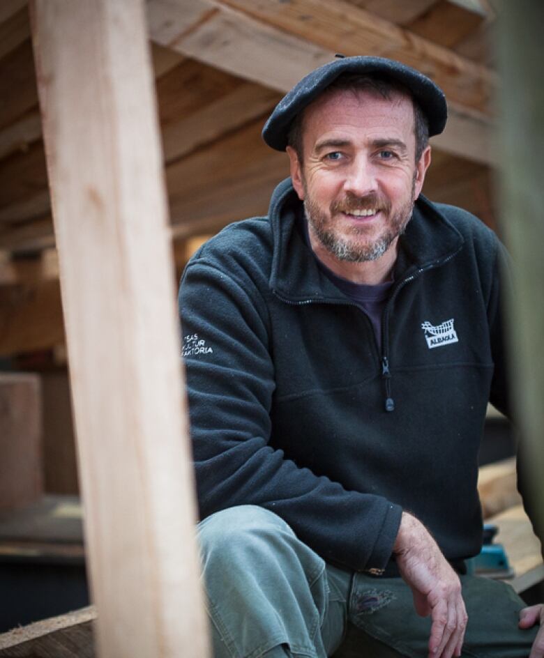 A man with a beard and a hat in a workship smiles at the camera