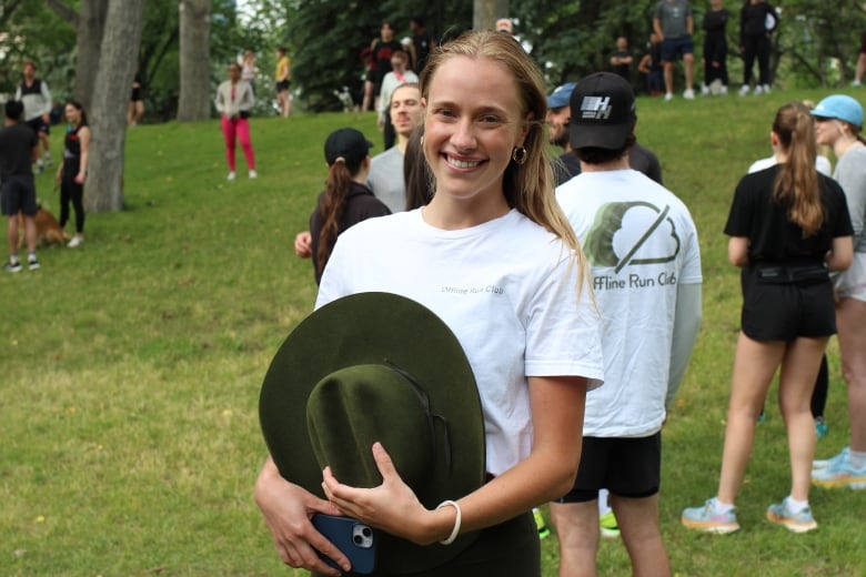 A woman wearing a white t-shirt and holding a cowboy hat poses in front of a group of runners. 