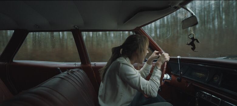 A woman sits in a car. She appears to be screaming. 