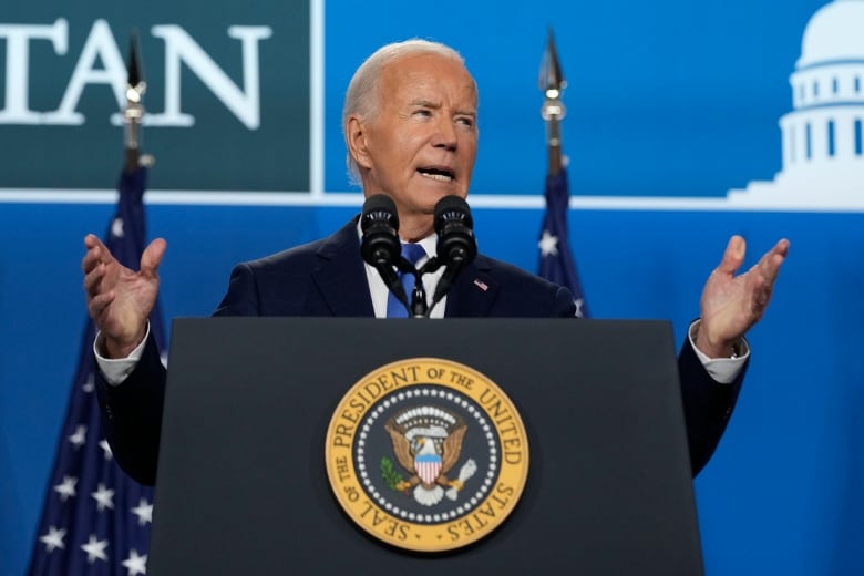 A man wearing a blue suit and blue tie speaks in front of a podium with the emblem of the U.S. presidency.