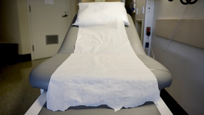 An exam table is seen from the foot of the bed, with white table paper covering it.