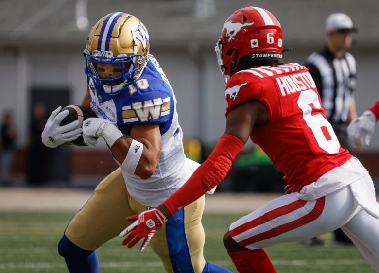 A football player in blue, white and gold runs while holding the ball. Another player in a red and white uniform chases.