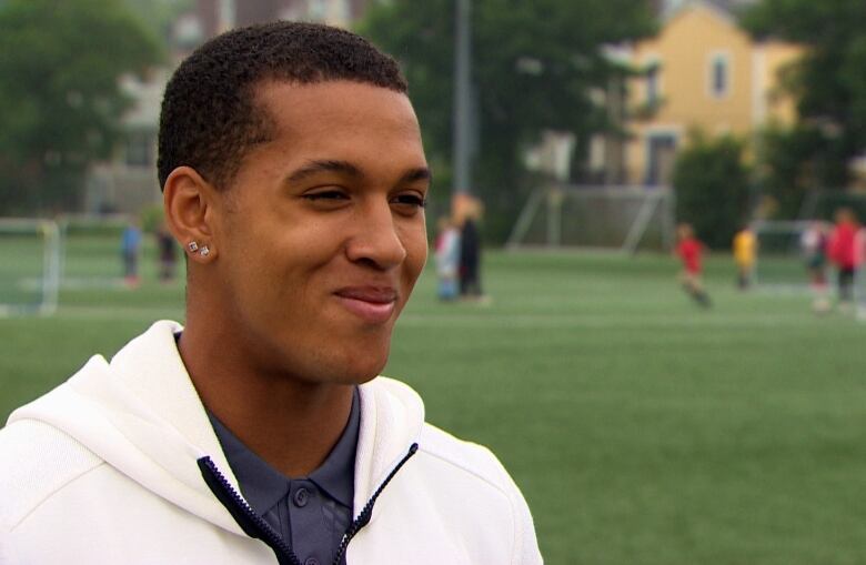 A man smiles while standing on a soccer field.