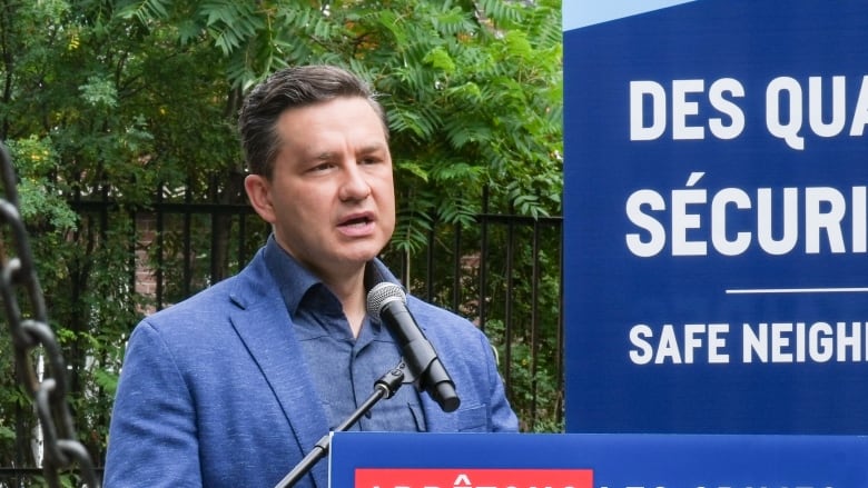 Pierre Poilievre stands behind a podium in an outdoor playground wearing a blue sport jacket. 