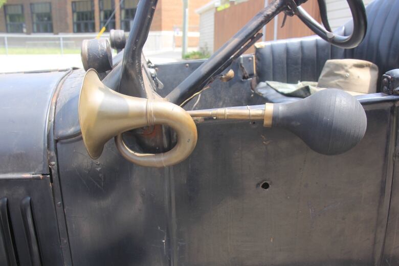 The side of an old black car is visible with a small hole in the side of the drivers door.