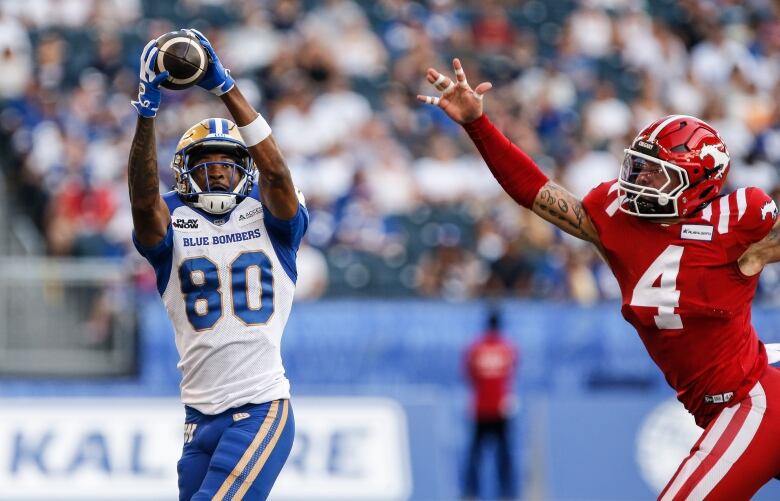 A man wearing a blue and white football uniform catches the ball as a player on the opposing team wearing red chases him. 