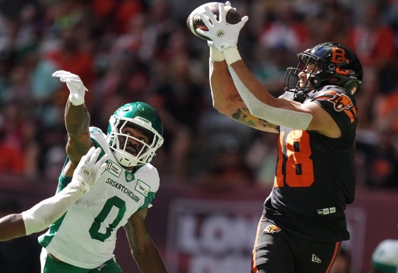 A man catches a football while another man tries to bat it away.