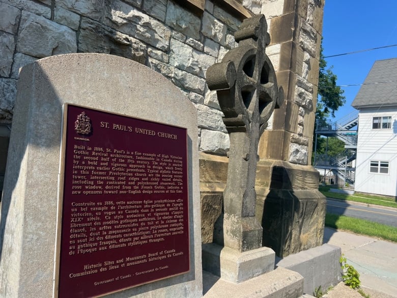 A stone cross and plaque are pictured outside of a church.