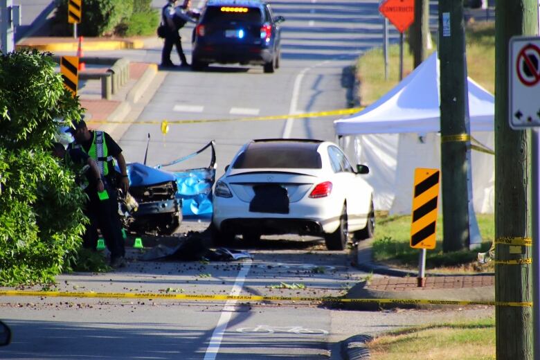 Two mangled cars are pictured behind crime tape on a sunny day.