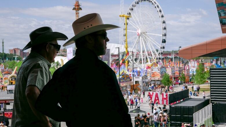 People look out across the midway at the Calgary Stampede wearing cowboy hats. 