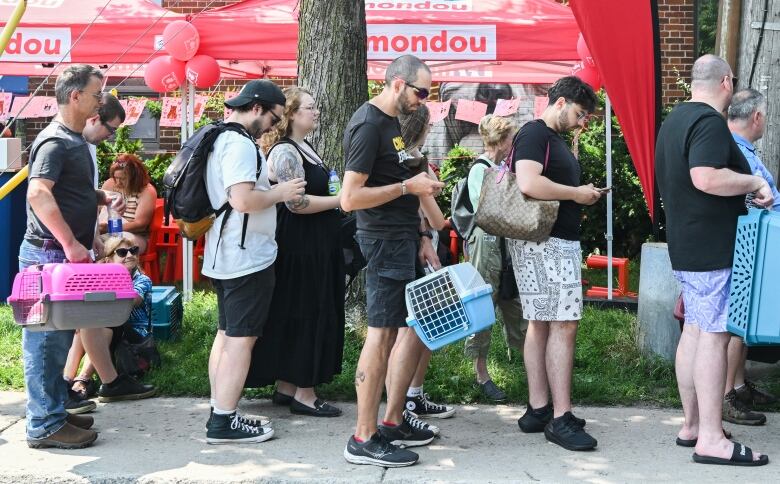 People waiting in a line outdoors, some of them holding crates. 