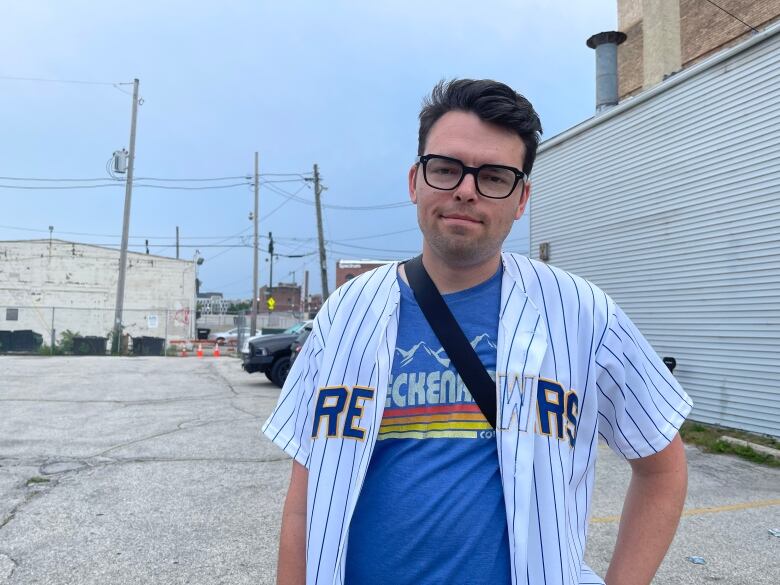 A man wearing a baseball jersey over a blue t-shirt is pictured.