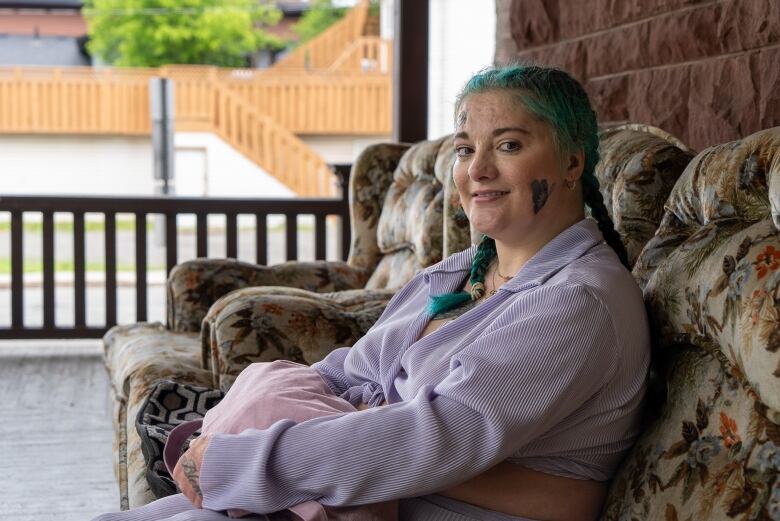 A person is seen sitting on a floral-patterned couch on a wraparound porch outside. They are smiling.