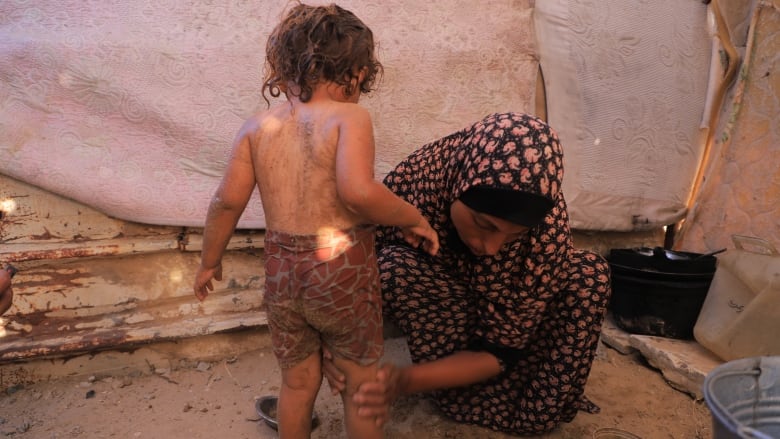 A woman wearing a red dress rubs sand on a girl's body