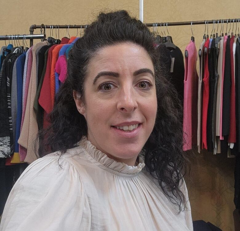 A profile of a woman with brown hair standing in front of a rack of cloths. 