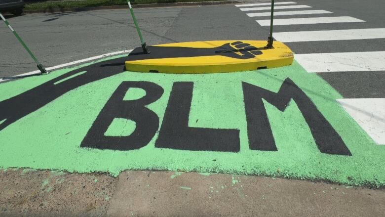 The letters BLM and a fist above it are over a green background are painted on a curb extension. 