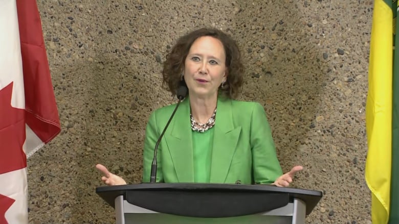 A woman in a green suit stands at a podium. 