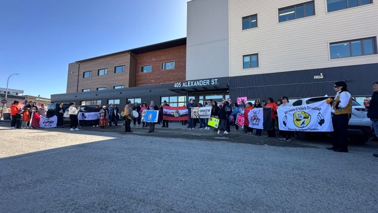 The photo shows several people, holding posters and signs, standing in front of a building in downtown Whitehorse. 