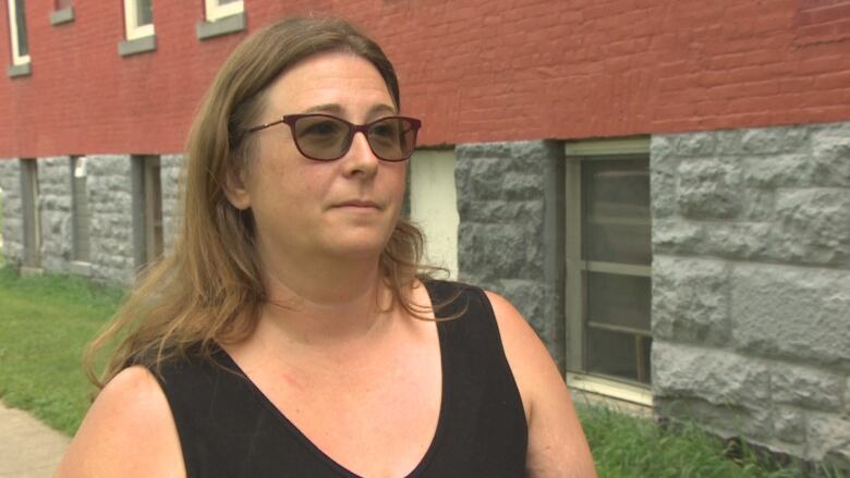 A woman stands outside wearing sunglasses. 