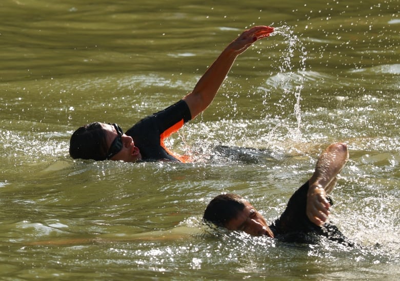 Two people are shown on the their sides in the water, with their arms in the air in a swimming motion.