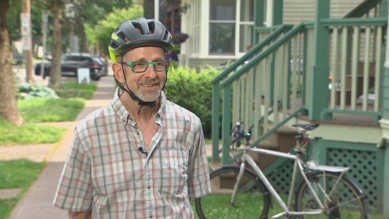 A man wearing a bike helmet stands in front of a bike on a residential street in Halifax. 