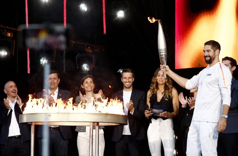 An athlete lights an Olympic flame while people clap.