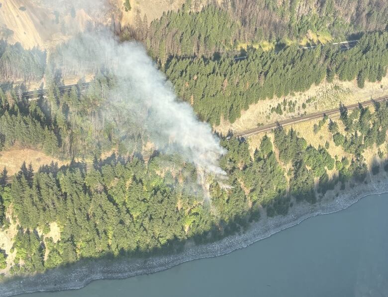 A smoky wildfire burns between a river and train tracks