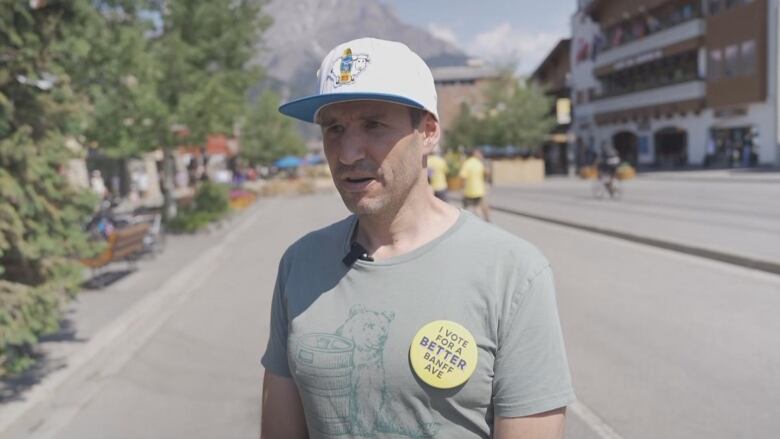 A man in a grey t-shirt and a baseball cap. he is wearing a button that reads 