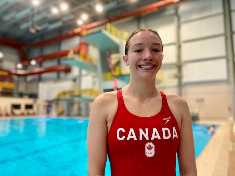 A woman in a red swimsuit reading Canada on the front stands in front of a pool. 