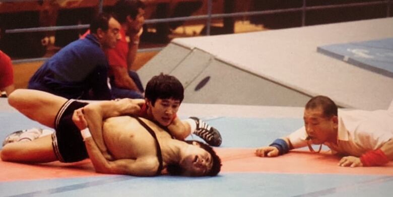 One wrestler pins another wrestler as a referee looks on intensely