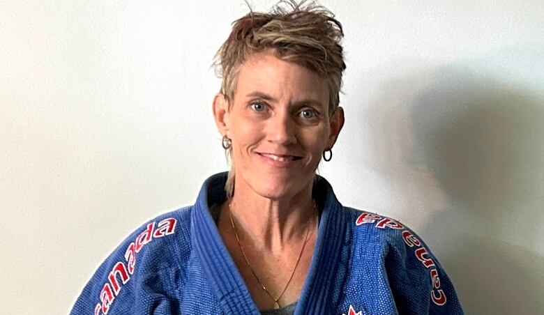 A person in a judo outfit and hoop earrings smiles at the camera