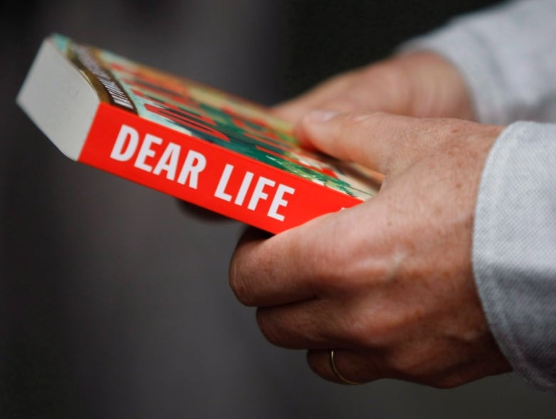 A closeup of someone holding a book is shown. On its spine the words 'Dear Life' are visible. 