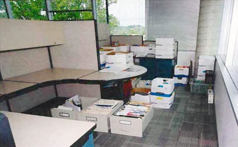 Stacks of cardboard boxes containing files and documents on the floor of an office cubicle.