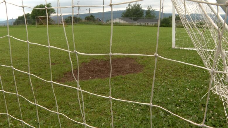 A large hole in the grass in a soccer net.