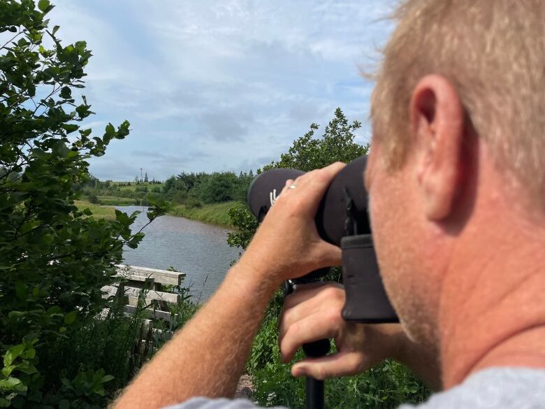 A man looks through a scope at an osprey platform 