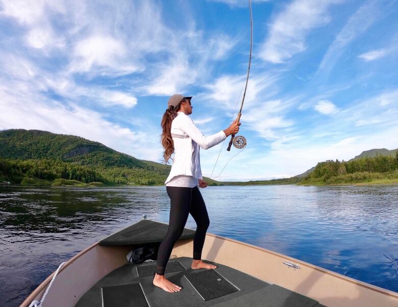 A woman in a white shirt and black pants stands barefoot in a boat.