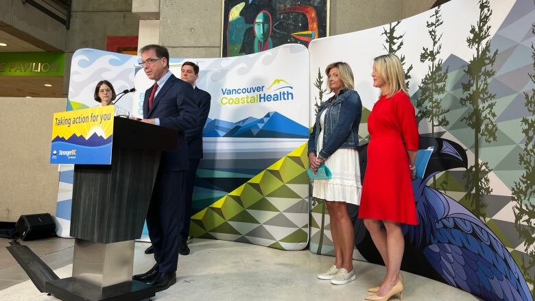 A man stands at a podium in the lobby of Vancouver General Hospital surrounded by four other people 