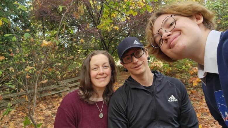 From left to right, a woman with long hair, a man with a hat and a teenager with short hair smiling. 