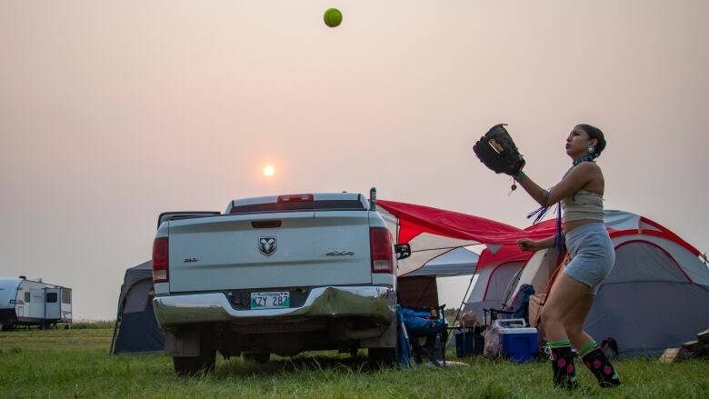 A girl with a mitt on her hand looks up at a ball in the air.