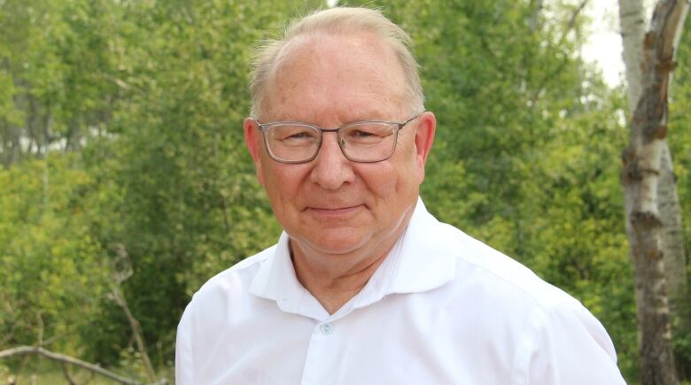 A man wearing glasses and a white button-up shirt smiles to the camera.