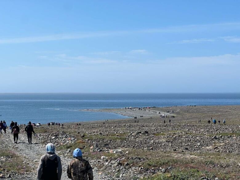 People walk down a gravel path near the water. 