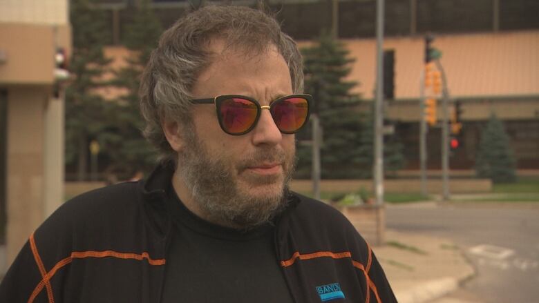 A man stands outside wearing orange sunglasses. 